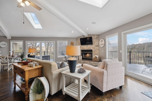 living room with ceiling fan, a stone fireplace, lofted ceiling with skylight, and dark wood-type flooring