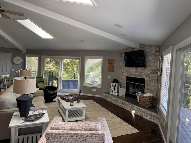 living room featuring wood-type flooring, lofted ceiling with beams, a stone fireplace, and a healthy amount of sunlight