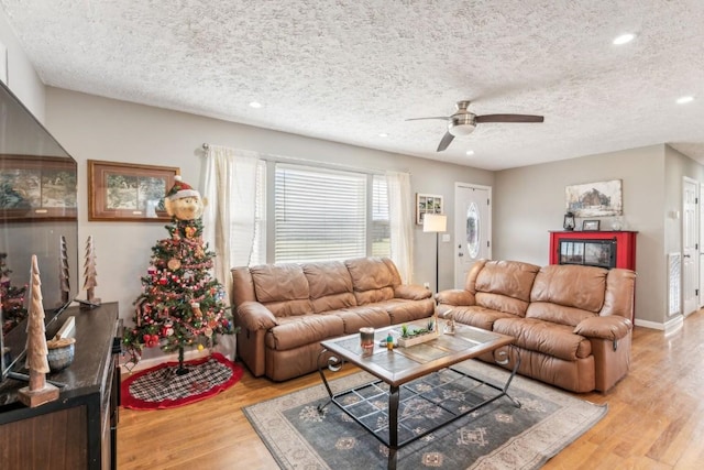 living room featuring ceiling fan, light hardwood / wood-style floors, and a textured ceiling