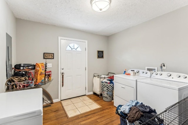 washroom with a textured ceiling, light wood-type flooring, electric panel, and washing machine and dryer