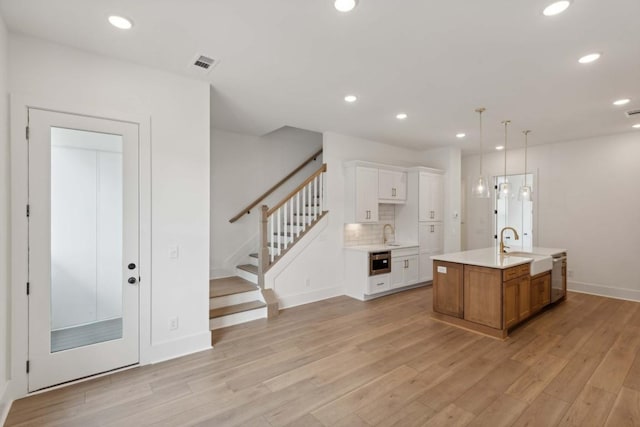 kitchen with backsplash, a kitchen island with sink, sink, light wood-type flooring, and white cabinetry