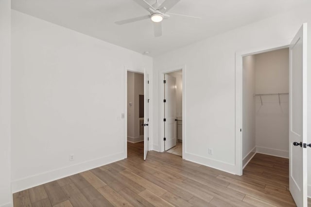 unfurnished bedroom with ceiling fan, a closet, a spacious closet, and light wood-type flooring