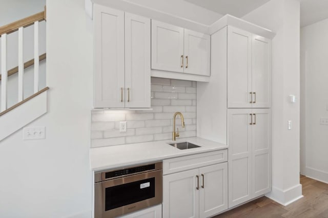 kitchen with hardwood / wood-style floors, backsplash, white cabinetry, and sink