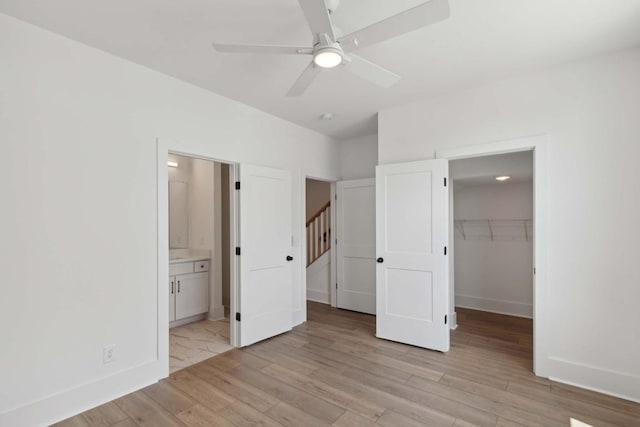 unfurnished bedroom featuring ceiling fan, a spacious closet, ensuite bathroom, light hardwood / wood-style floors, and a closet