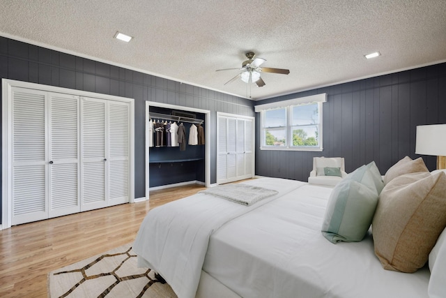 bedroom with multiple closets, ceiling fan, light hardwood / wood-style floors, and a textured ceiling