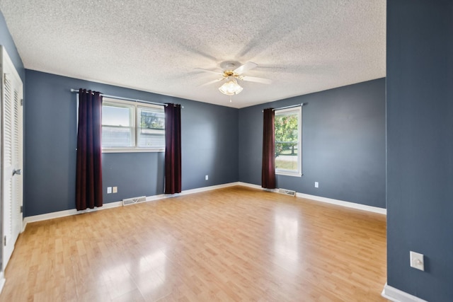 spare room featuring a textured ceiling, light wood-type flooring, and a healthy amount of sunlight