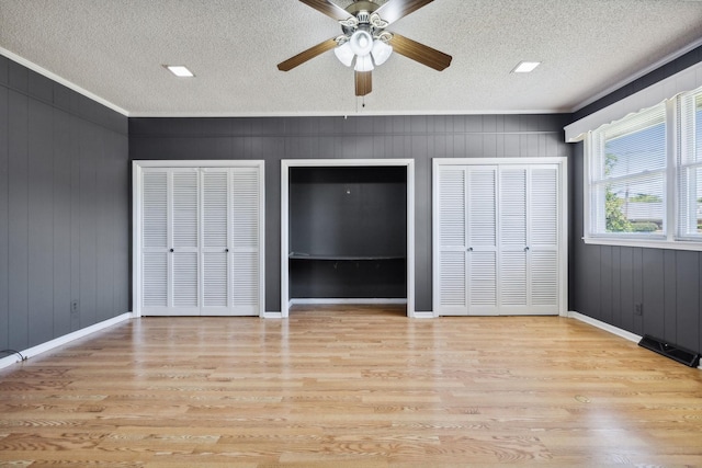 unfurnished bedroom with ceiling fan, light wood-type flooring, crown molding, and multiple closets