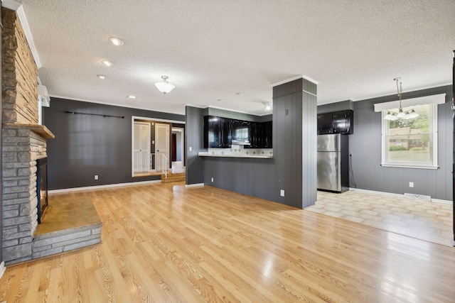 unfurnished living room featuring a fireplace, a textured ceiling, a chandelier, and light hardwood / wood-style flooring