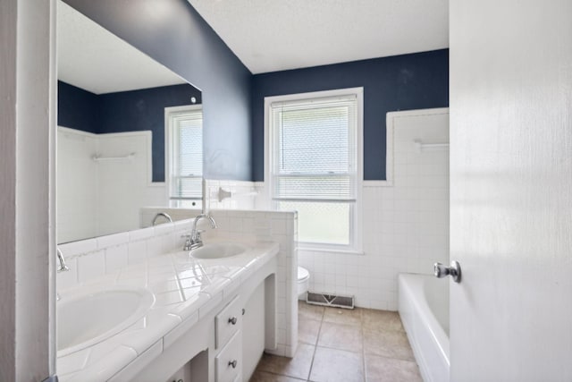 bathroom with tile patterned flooring, a textured ceiling, toilet, vanity, and tile walls