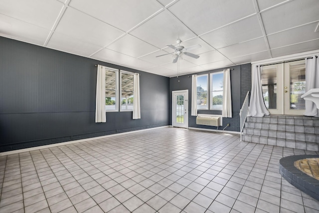 empty room featuring ceiling fan, french doors, a wall unit AC, a paneled ceiling, and light tile patterned flooring