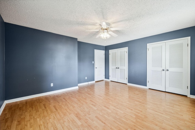 unfurnished bedroom with multiple closets, ceiling fan, light hardwood / wood-style floors, and a textured ceiling