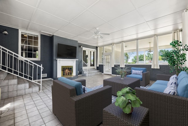 tiled living room with an outdoor brick fireplace and ceiling fan