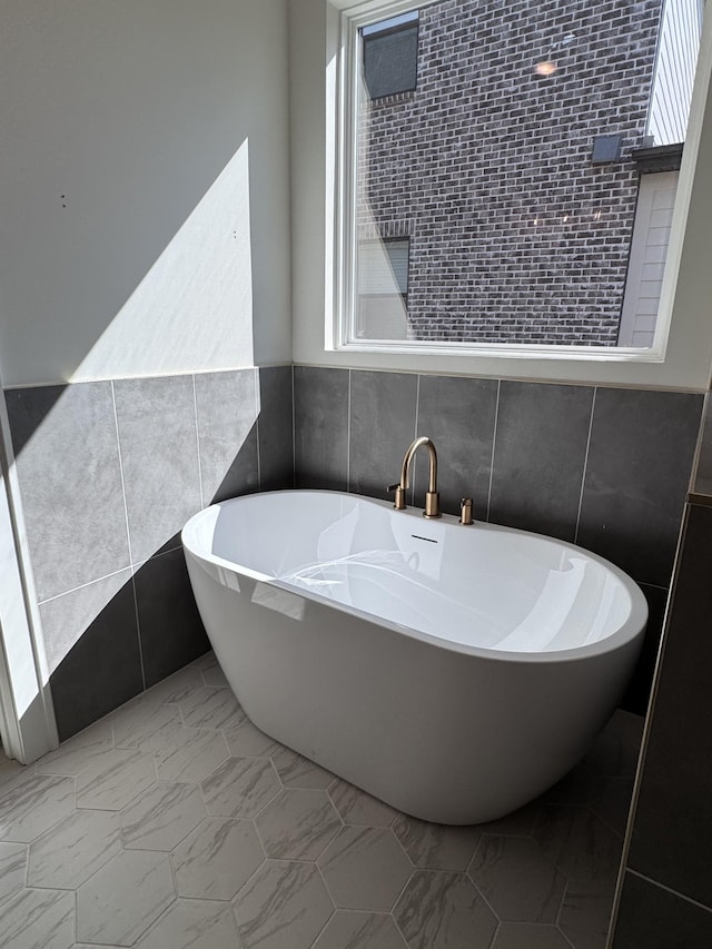 full bath featuring tile walls, marble finish floor, and a freestanding bath