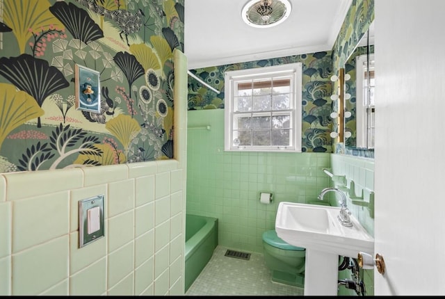 bathroom with a washtub, tile patterned flooring, toilet, crown molding, and tile walls