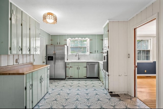 kitchen featuring green cabinetry, wooden walls, appliances with stainless steel finishes, ornamental molding, and sink