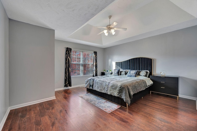 bedroom featuring a textured ceiling, dark hardwood / wood-style flooring, a raised ceiling, and ceiling fan