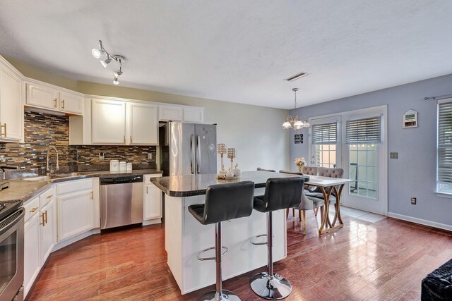 kitchen featuring sink, hanging light fixtures, stainless steel appliances, white cabinets, and hardwood / wood-style flooring