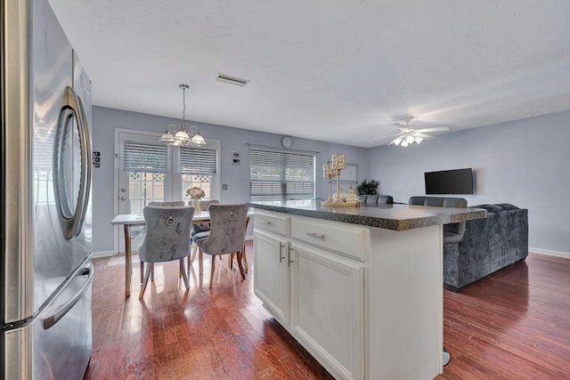 kitchen with dark hardwood / wood-style flooring, a kitchen island, white cabinets, stainless steel refrigerator, and hanging light fixtures