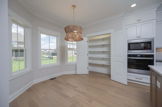 unfurnished dining area featuring light wood-type flooring, ornamental molding, and a wealth of natural light