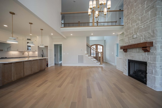 unfurnished living room with light hardwood / wood-style floors, a towering ceiling, a fireplace, and an inviting chandelier