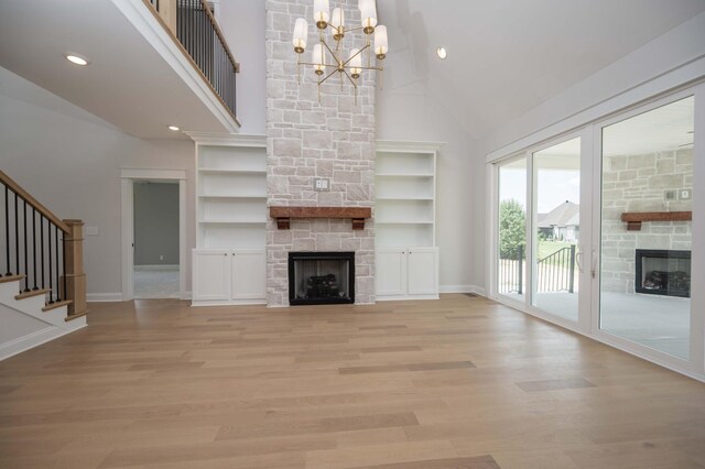 unfurnished living room with light wood-type flooring, a fireplace, high vaulted ceiling, and an inviting chandelier