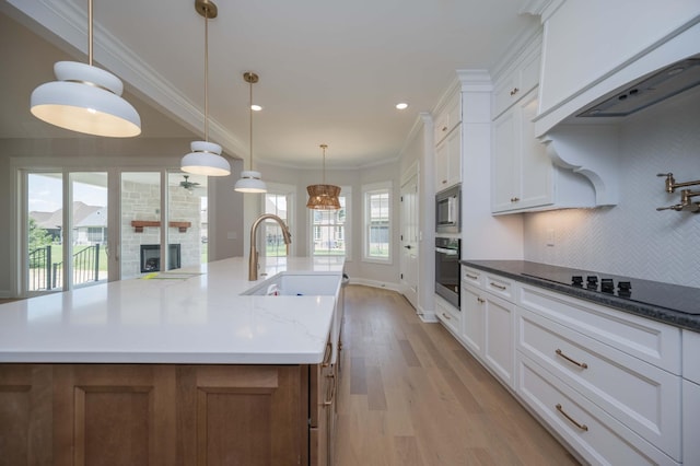 kitchen with light wood-type flooring, stainless steel appliances, sink, white cabinetry, and an island with sink