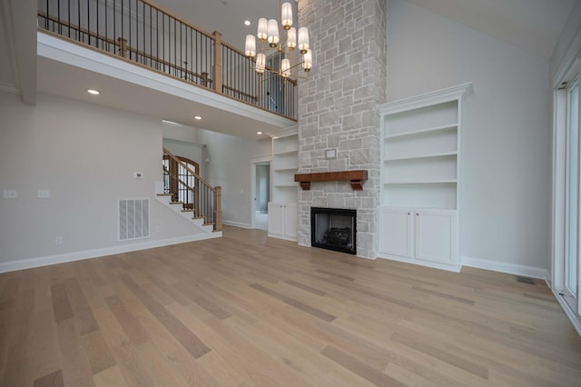 unfurnished living room featuring built in shelves, a stone fireplace, light hardwood / wood-style flooring, high vaulted ceiling, and a chandelier