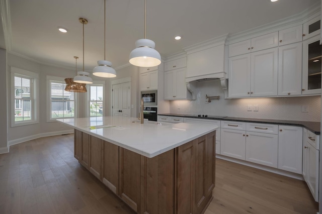 kitchen featuring a kitchen island with sink, decorative light fixtures, oven, white cabinetry, and stainless steel microwave