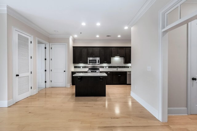 kitchen with sink, appliances with stainless steel finishes, light wood-type flooring, a kitchen island, and ornamental molding