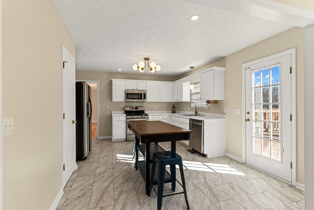 kitchen featuring sink, white cabinetry, appliances with stainless steel finishes, a textured ceiling, and a chandelier