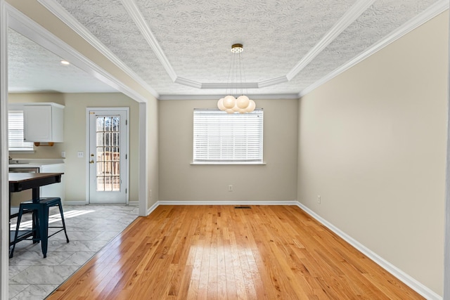 unfurnished dining area with light wood-type flooring, a tray ceiling, and ornamental molding