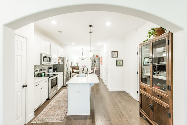 kitchen with white cabinetry, sink, stainless steel appliances, an island with sink, and decorative light fixtures