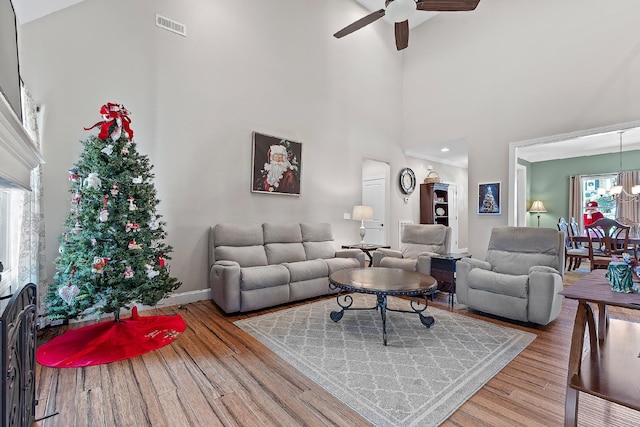 living room featuring a high ceiling, ceiling fan with notable chandelier, a wealth of natural light, and wood-type flooring