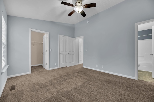 unfurnished bedroom featuring lofted ceiling, ensuite bathroom, carpet flooring, ceiling fan, and multiple windows