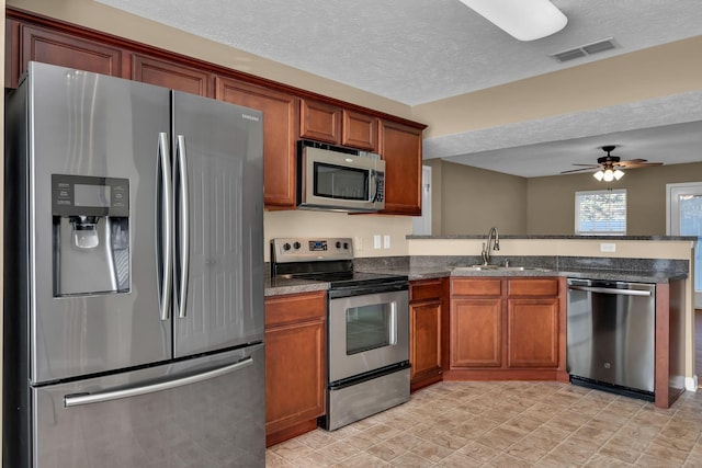 kitchen with a textured ceiling, stainless steel appliances, ceiling fan, and sink