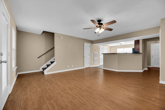 unfurnished living room featuring ceiling fan with notable chandelier and hardwood / wood-style flooring