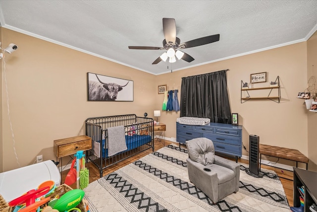 bedroom with wood-type flooring, crown molding, ceiling fan, a textured ceiling, and a crib