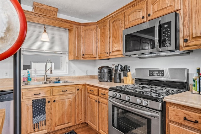 kitchen with a textured ceiling, stainless steel appliances, hanging light fixtures, and sink