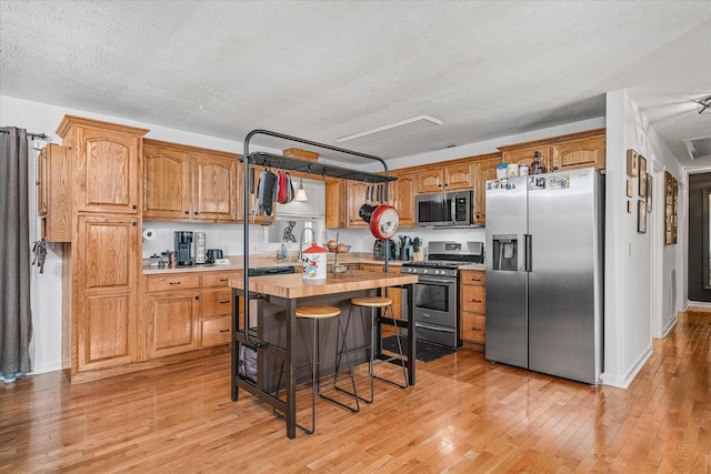 kitchen with butcher block counters, light wood-type flooring, a textured ceiling, and appliances with stainless steel finishes