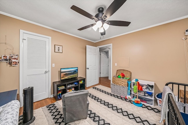 playroom with ceiling fan, light hardwood / wood-style floors, a textured ceiling, and ornamental molding