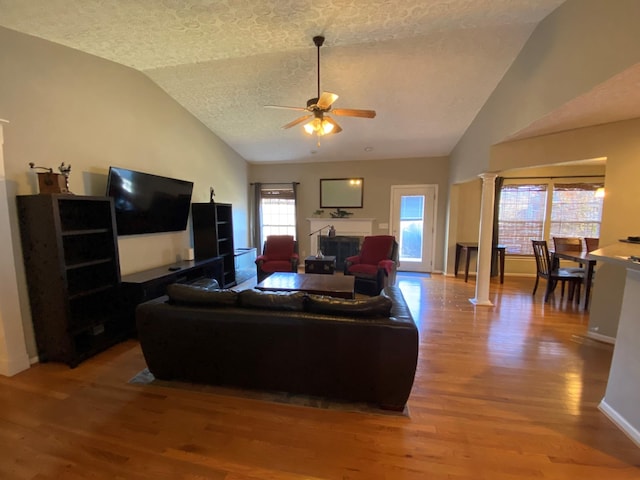 living room featuring ceiling fan, decorative columns, hardwood / wood-style floors, lofted ceiling, and a textured ceiling