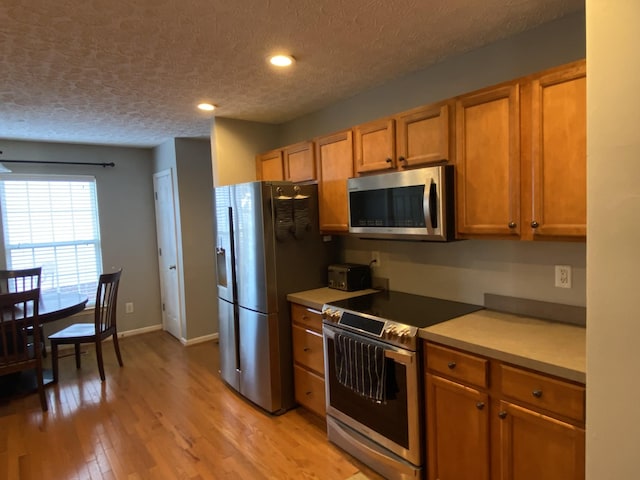 kitchen with appliances with stainless steel finishes, light wood-type flooring, and a textured ceiling