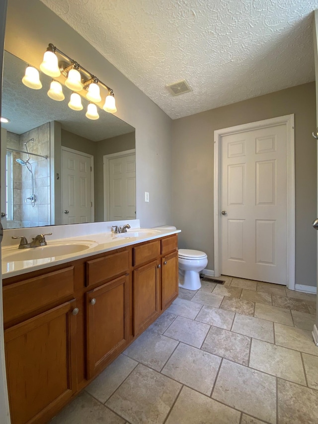 bathroom featuring toilet, vanity, a textured ceiling, and tiled shower