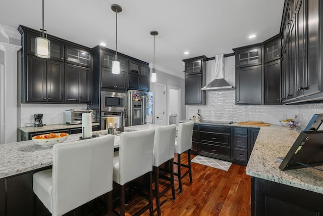 kitchen featuring pendant lighting, a breakfast bar, dark wood-type flooring, wall chimney exhaust hood, and appliances with stainless steel finishes