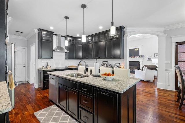 kitchen featuring a kitchen island with sink, wall chimney range hood, sink, ornamental molding, and decorative light fixtures