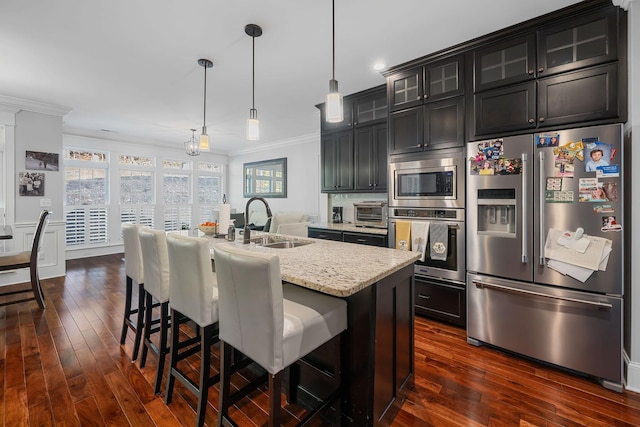 kitchen featuring decorative light fixtures, stainless steel appliances, a breakfast bar, and an island with sink