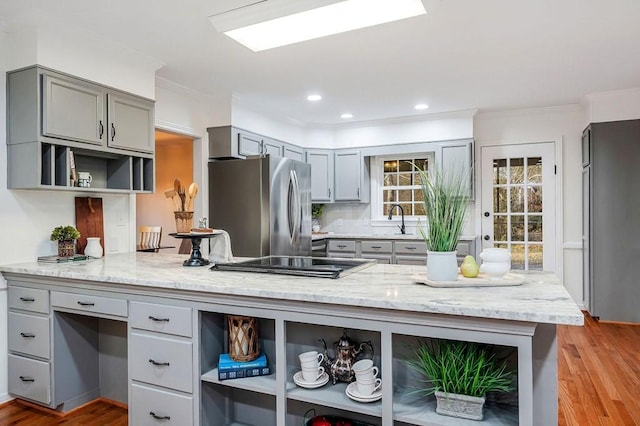 kitchen featuring kitchen peninsula, stainless steel appliances, light hardwood / wood-style flooring, and light stone counters