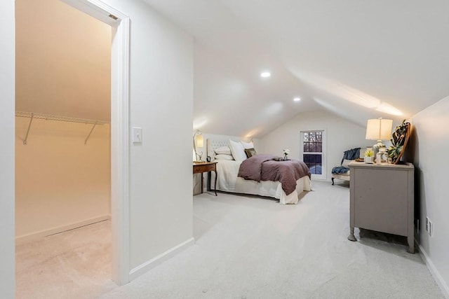 bedroom with a walk in closet, a closet, light colored carpet, and vaulted ceiling