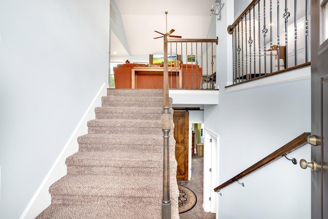 stairway with ceiling fan, a barn door, and a high ceiling