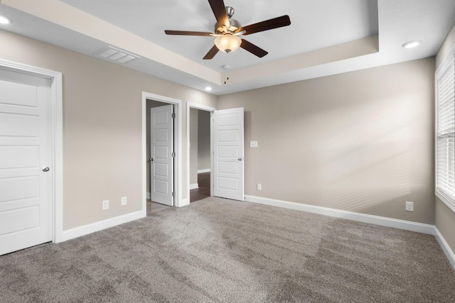 unfurnished bedroom featuring carpet, ceiling fan, and a raised ceiling